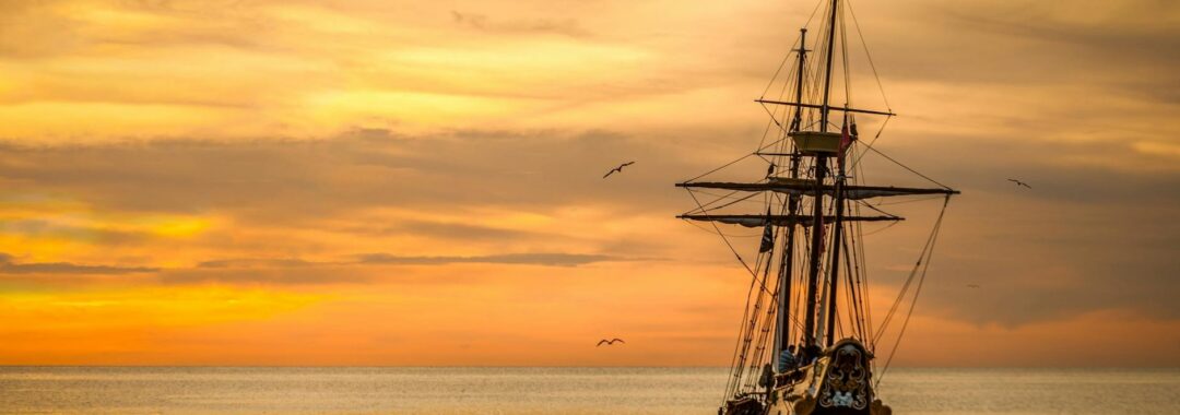 a pirate ship sailing on sea during golden hour